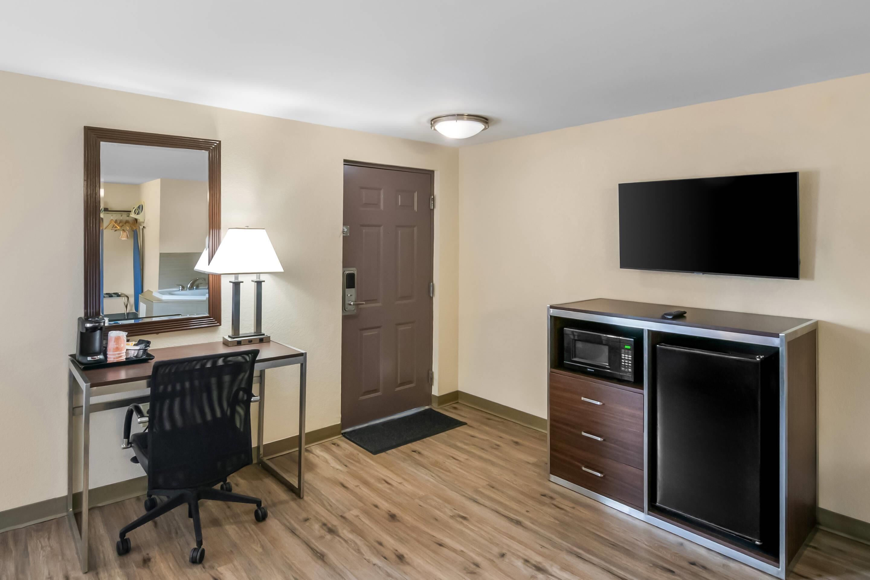 Una habitación de hotel con escritorio, silla, espejo, televisor, microondas y refrigerador.