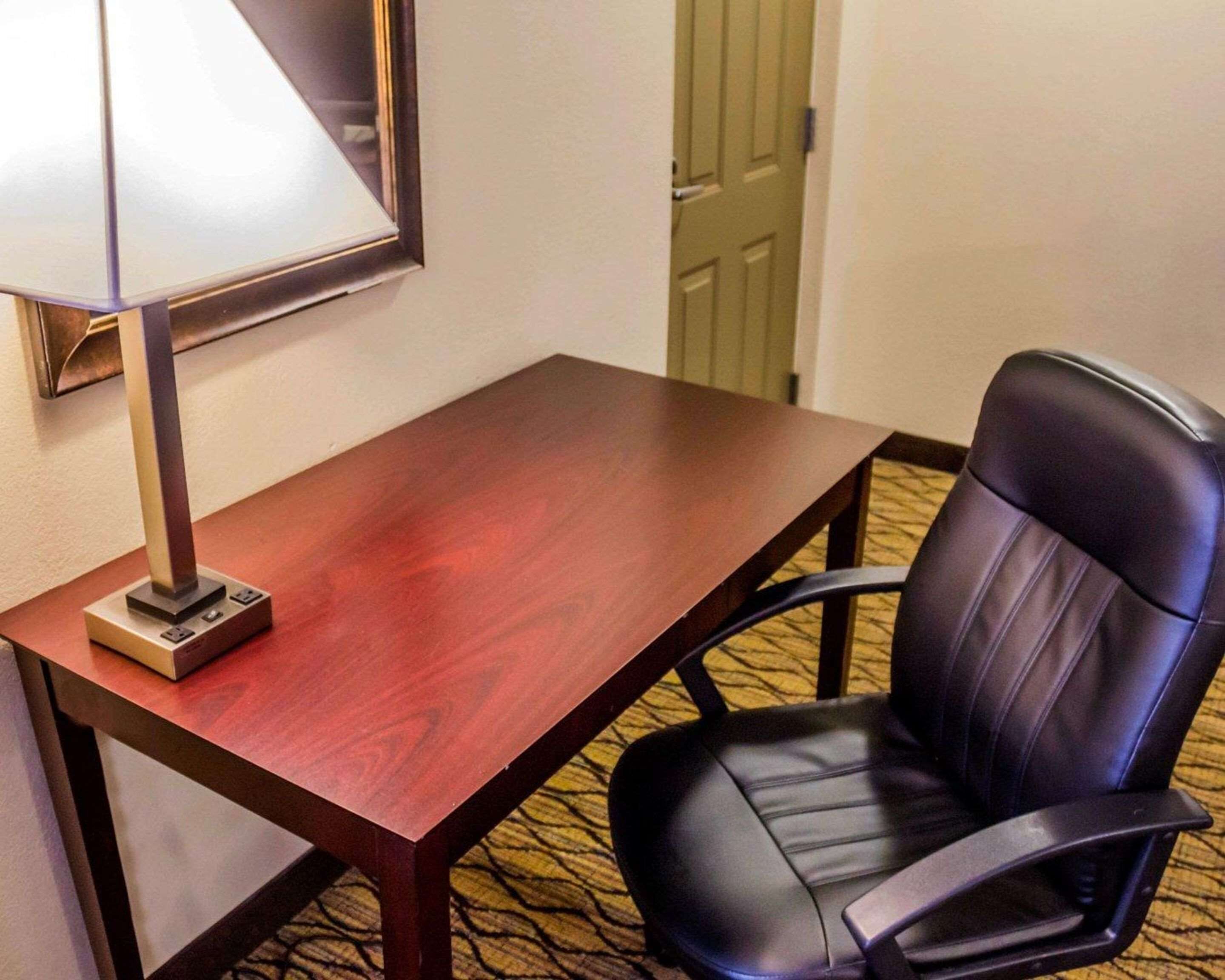 A hotel room with a wooden desk, a black leather chair, and a lamp.