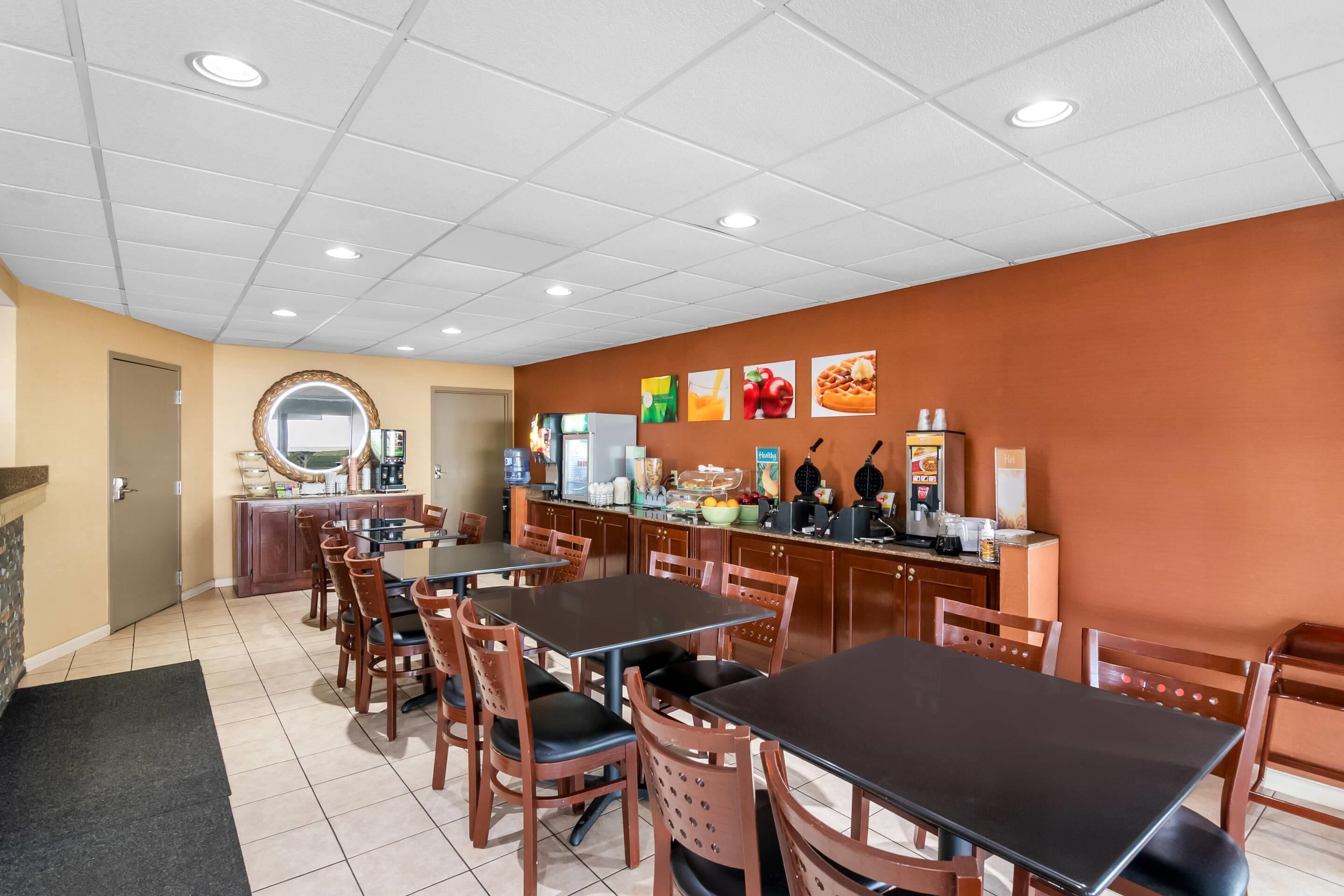 A restaurant with multiple tables and chairs, a counter with food and drink items, and a wall with pictures of food.