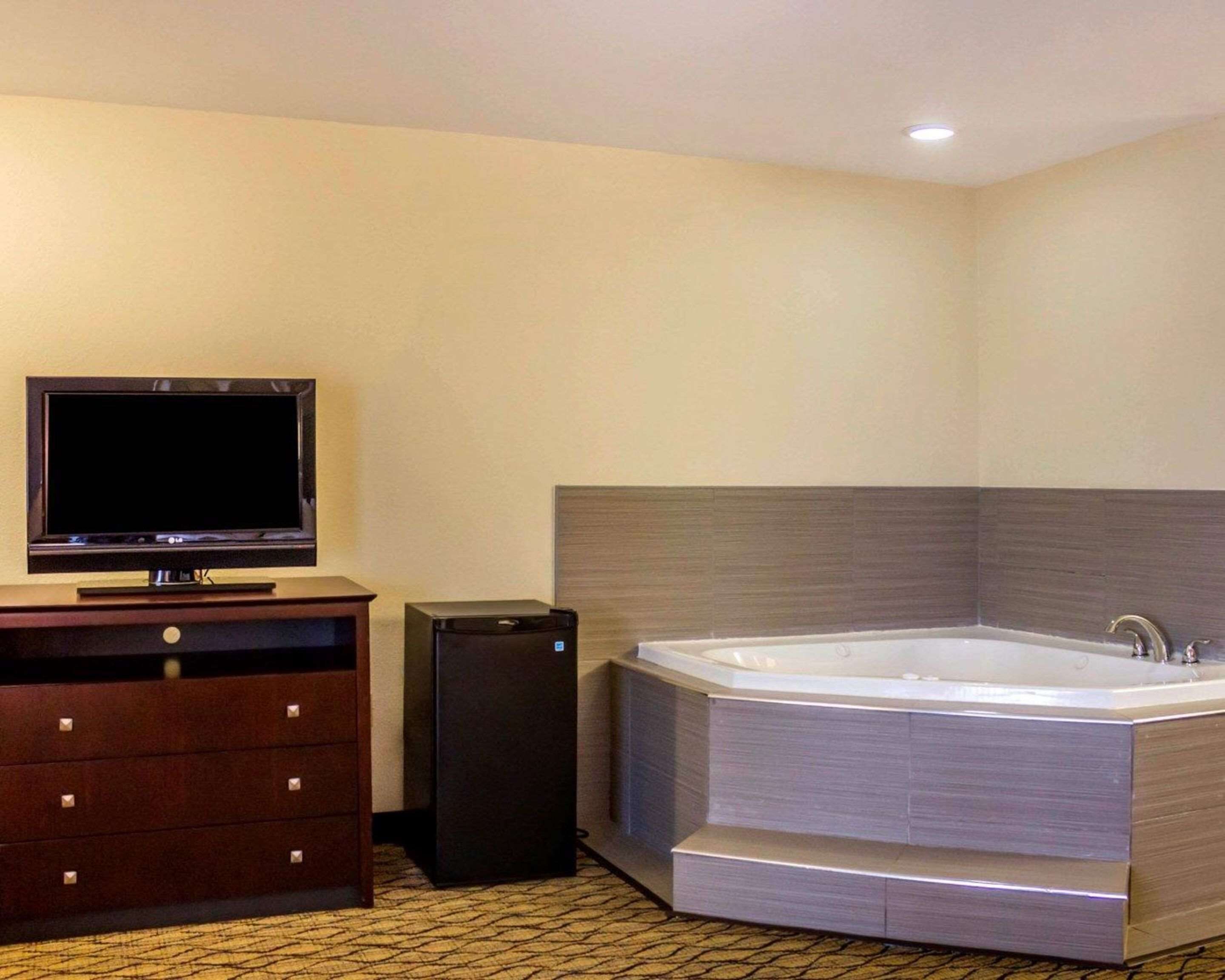 A bathroom with a large bathtub, a television on a wooden cabinet, and a black speaker.
