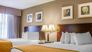 A hotel room with two beds, a nightstand with a lamp, and framed artwork on the wall.