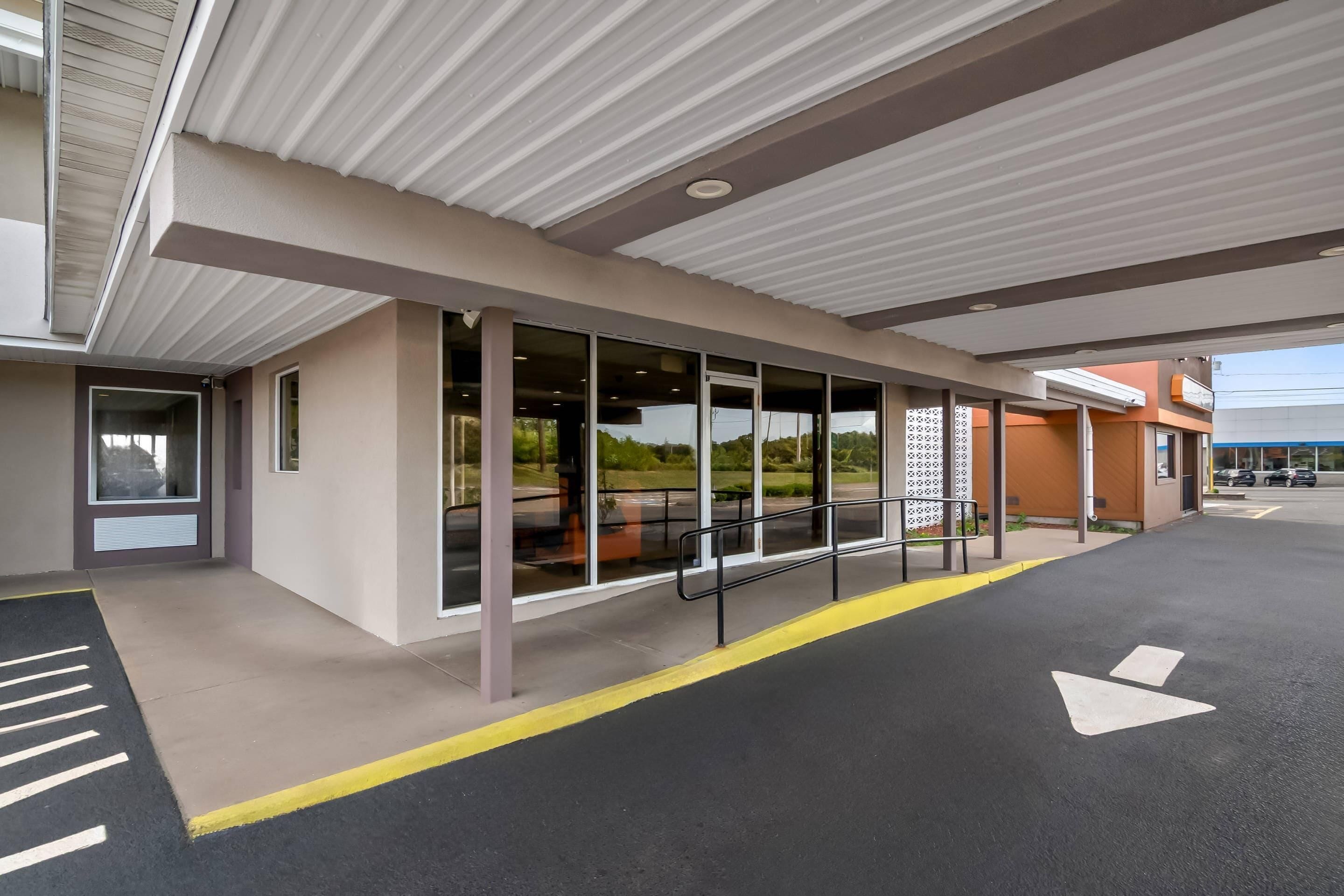 A modern building with large windows, a covered walkway, and directional arrows on the pavement.