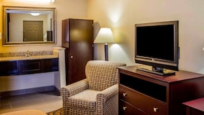 A hotel room with a bathroom, a TV, a chair, and a desk.