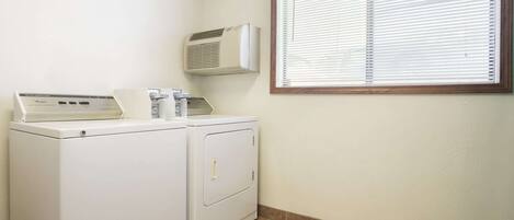 A laundry area with a front-loading washer and dryer, a wall-mounted air conditioner, and a window with blinds.