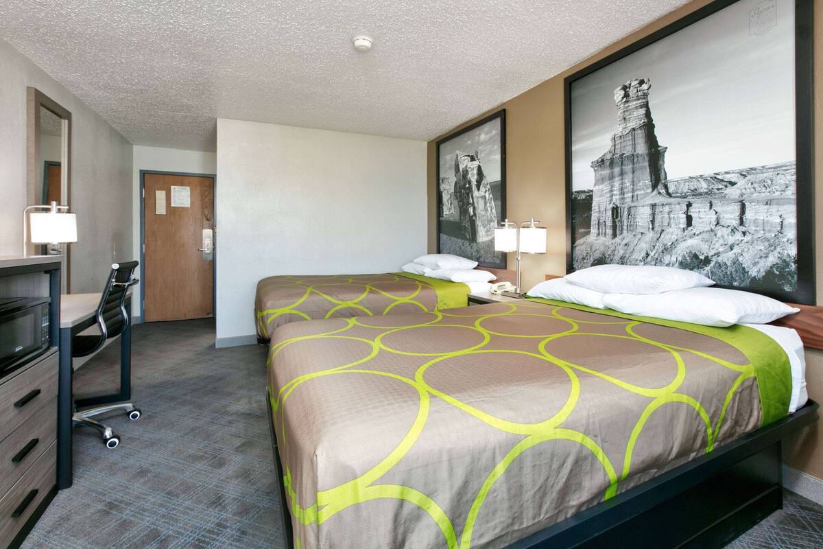 Une chambre d’hôtel avec un grand lit, un bureau avec une chaise, un miroir et deux lampes fixées au mur.