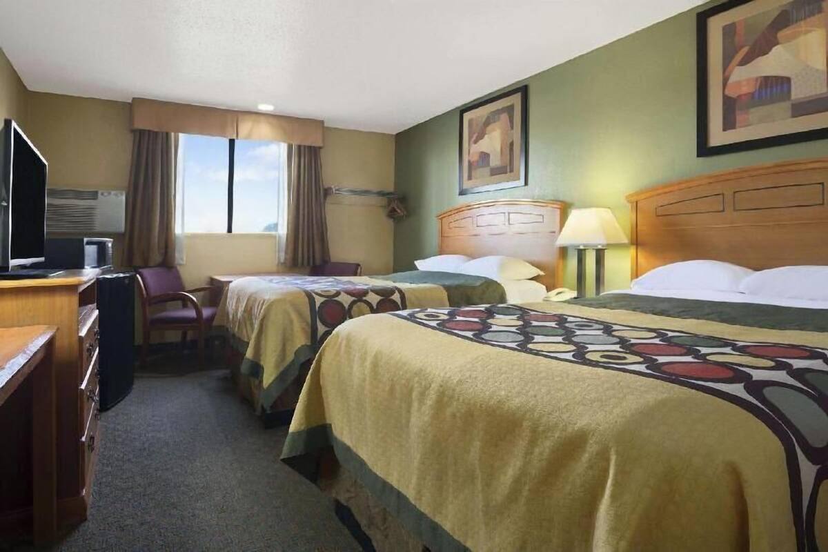 Une chambre d’hôtel avec deux lits, un bureau avec un ordinateur, une chaise et une fenêtre avec des rideaux.