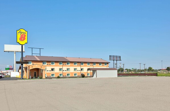Un motel Super 8 con un edificio de dos pisos, un estacionamiento y un cielo azul despejado.