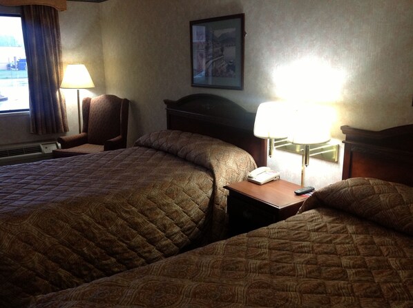 A hotel room with two beds, a nightstand with a lamp, a telephone, and a painting on the wall. - Colonial Inn & Suites /Airport/Graceland (Memphis)
