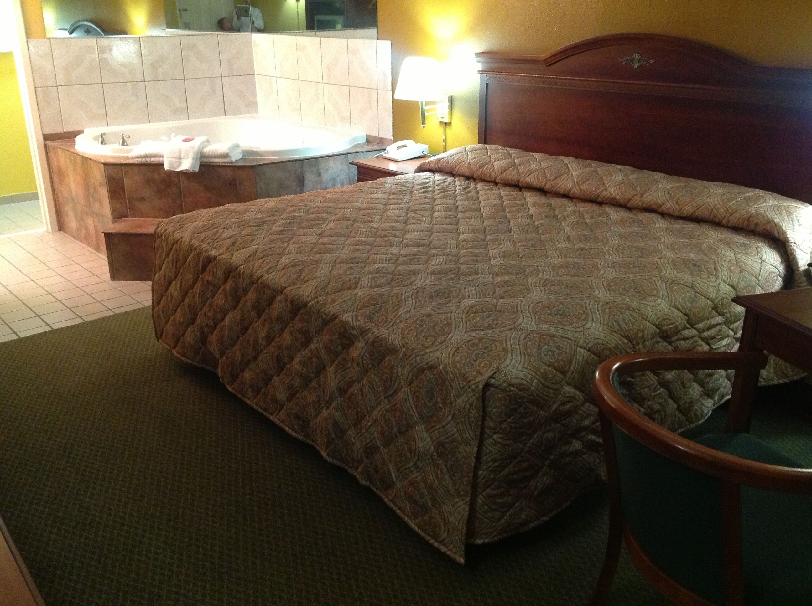 A hotel room with a large bed, a separate bathtub, and a wooden headboard.