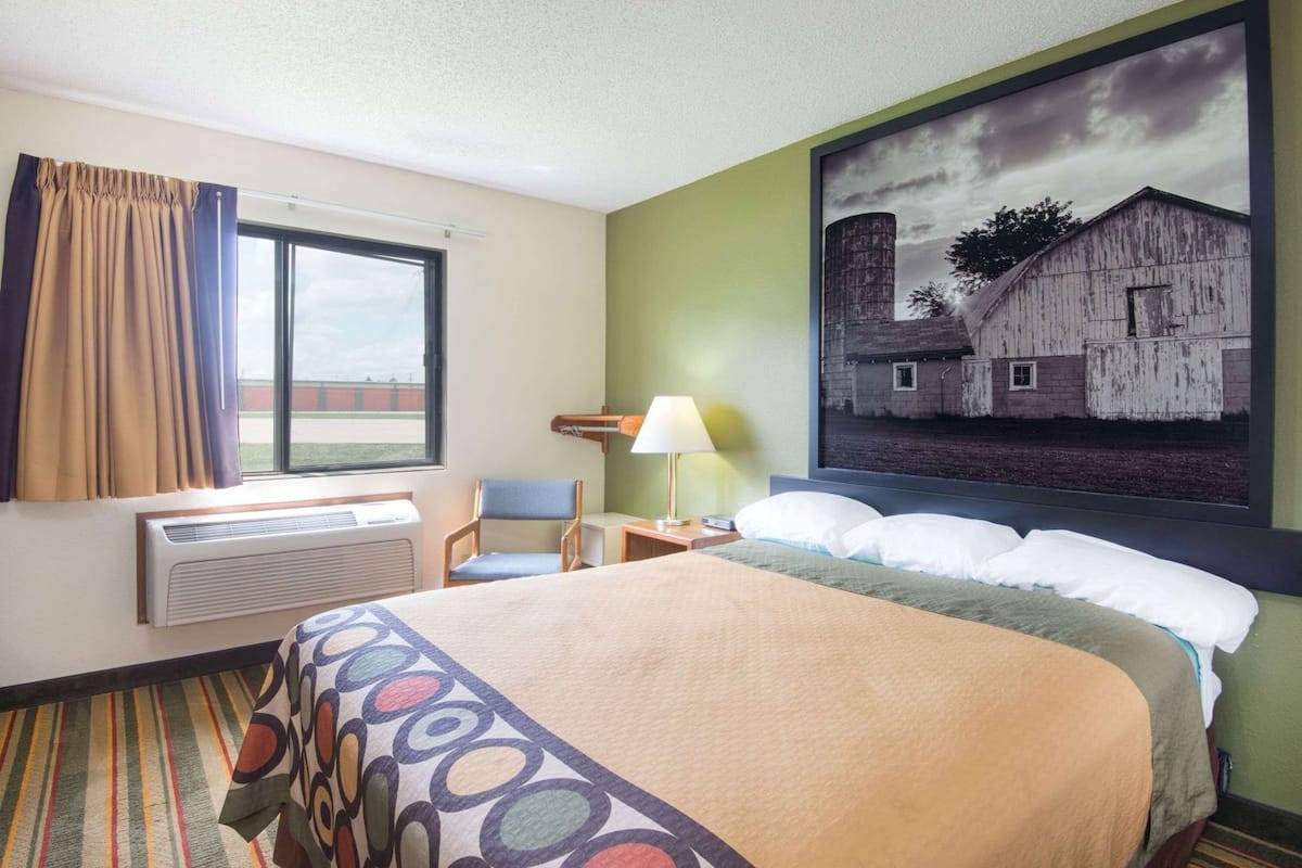 Una habitación de hotel con una cama, una silla, un escritorio, una lámpara y un ventanal grande.