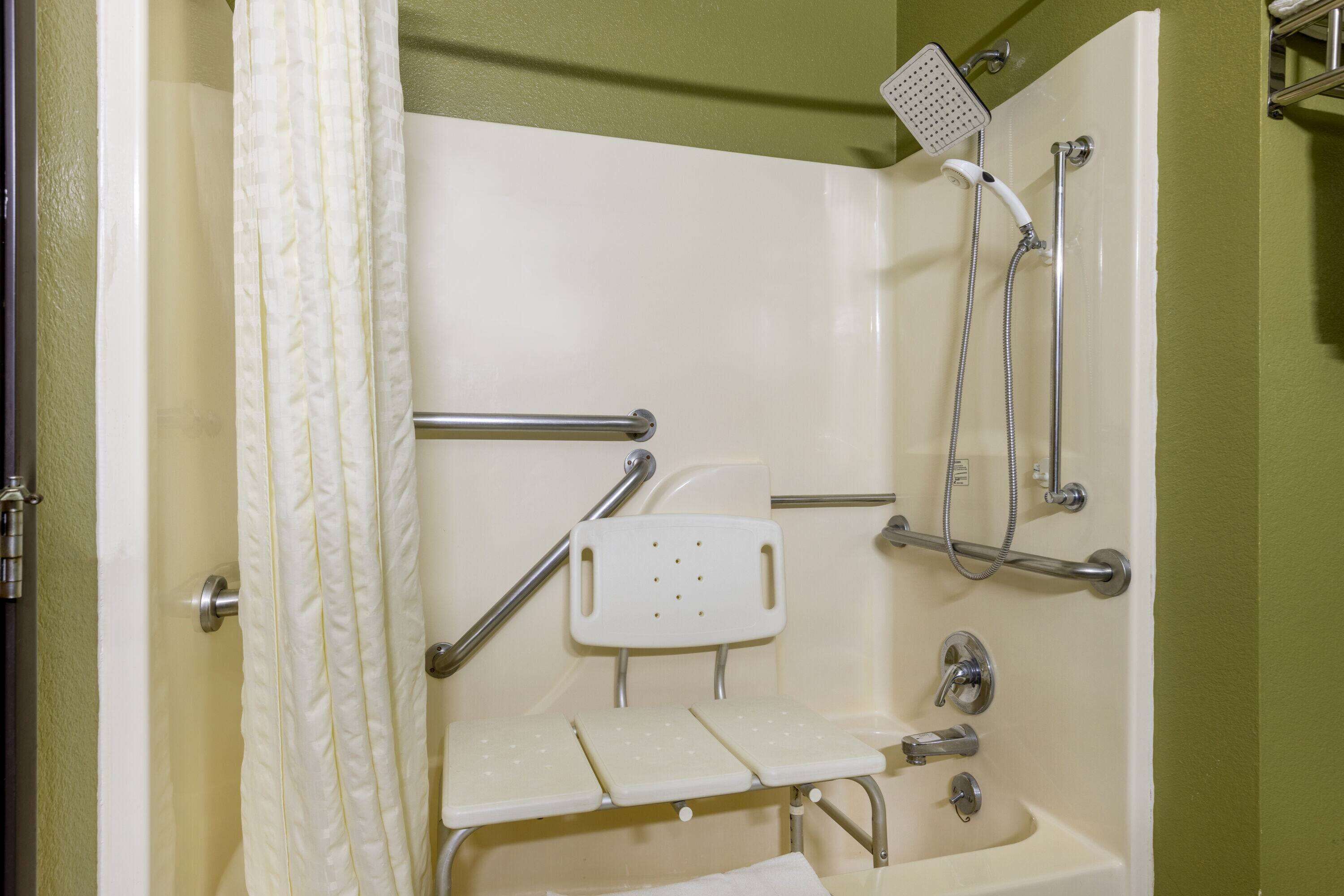 Une salle de bain équipée d’une douche, de barres d’appui, d’un banc accessible aux personnes en fauteuil roulant et d’un lavabo.