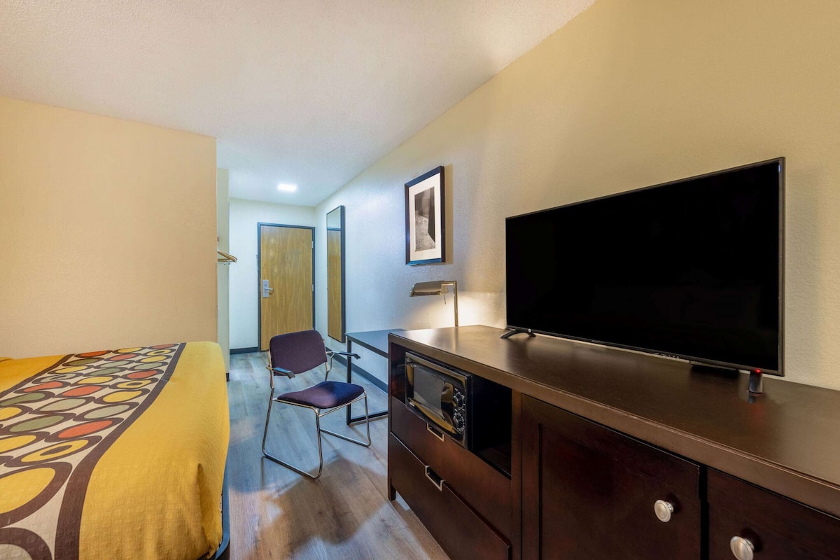 Habitación de hotel con cama, escritorio con televisor, silla y kitchenette pequeña.