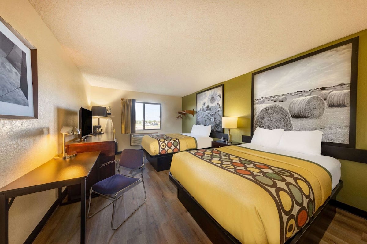 Habitación de hotel con dos camas, un escritorio, una silla, un televisor y un ventanal grande.