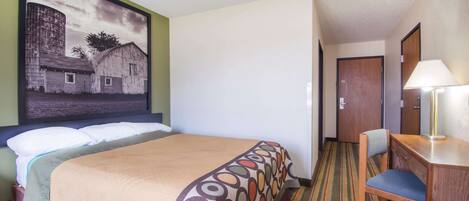 A hotel room with a bed, a desk, a chair, a lamp, and a painting on the wall.