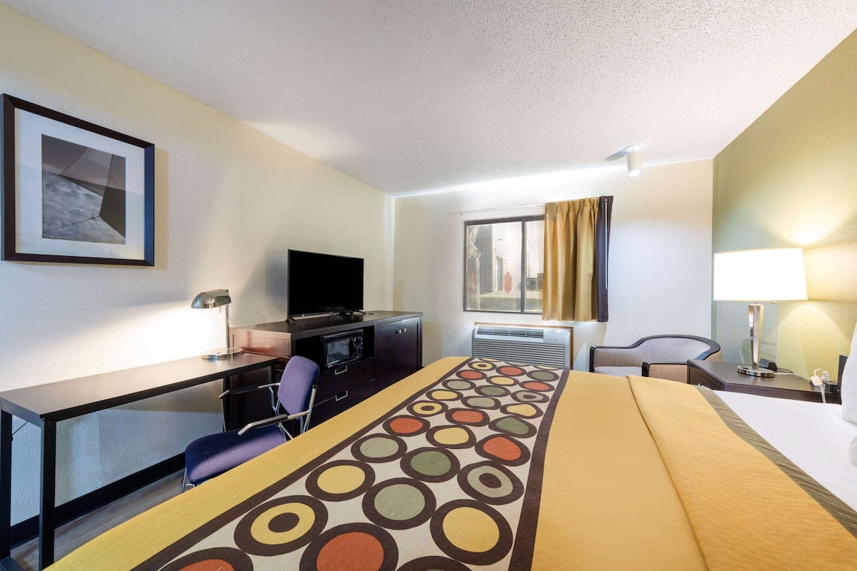Una habitación de hotel con cama, escritorio, silla, televisor y ventana con cortinas.