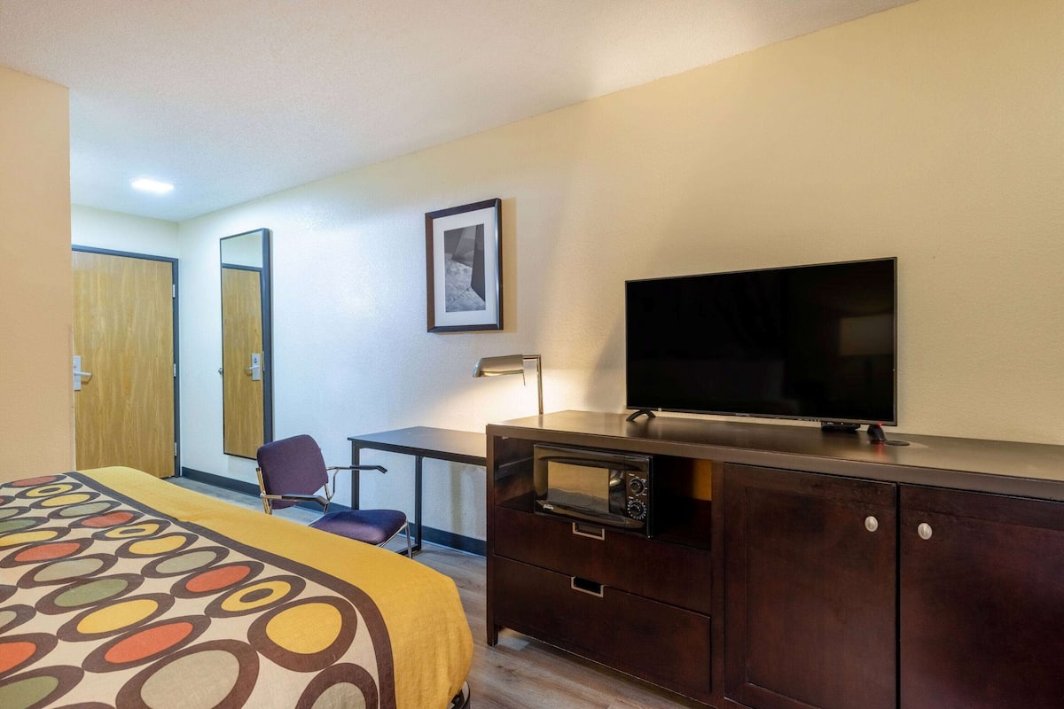Habitación de hotel con una cama, un escritorio, televisor, microondas y una silla.