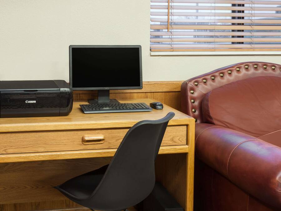 A wooden desk with a Canon printer, a monitor, a keyboard, and a mouse. There is a black office chair in front of the desk.