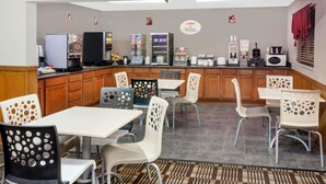Un área de desayuno con mostrador, máquinas de café y asientos.