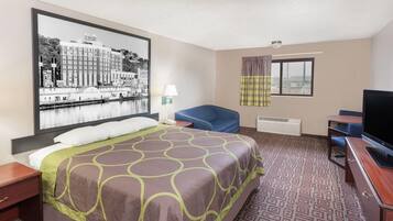 A hotel room with a bed, a desk, a chair, a television, and a large framed picture on the wall.