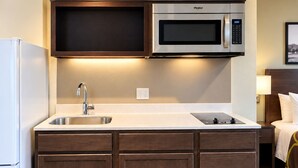 A compact kitchen with a built-in microwave, a stainless steel sink, and wooden cabinetry. - Super 8 by Wyndham Muscatine (Muscatine)