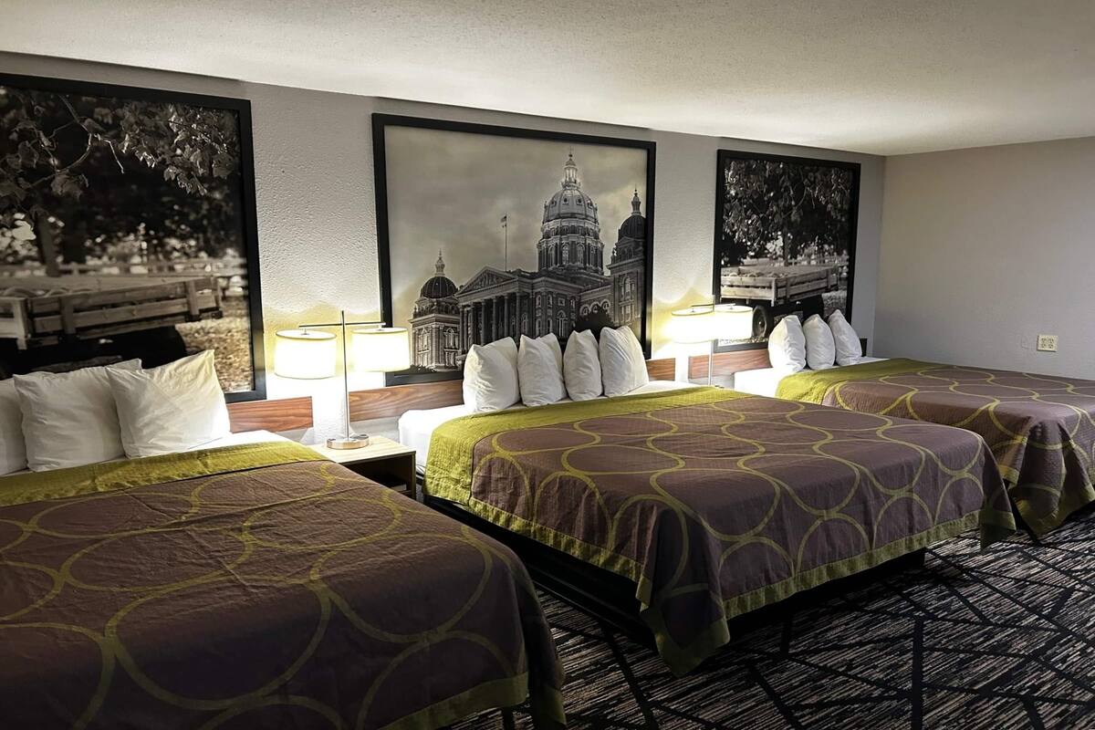 A hotel room with two beds, a large framed picture of a building, and a patterned carpet.