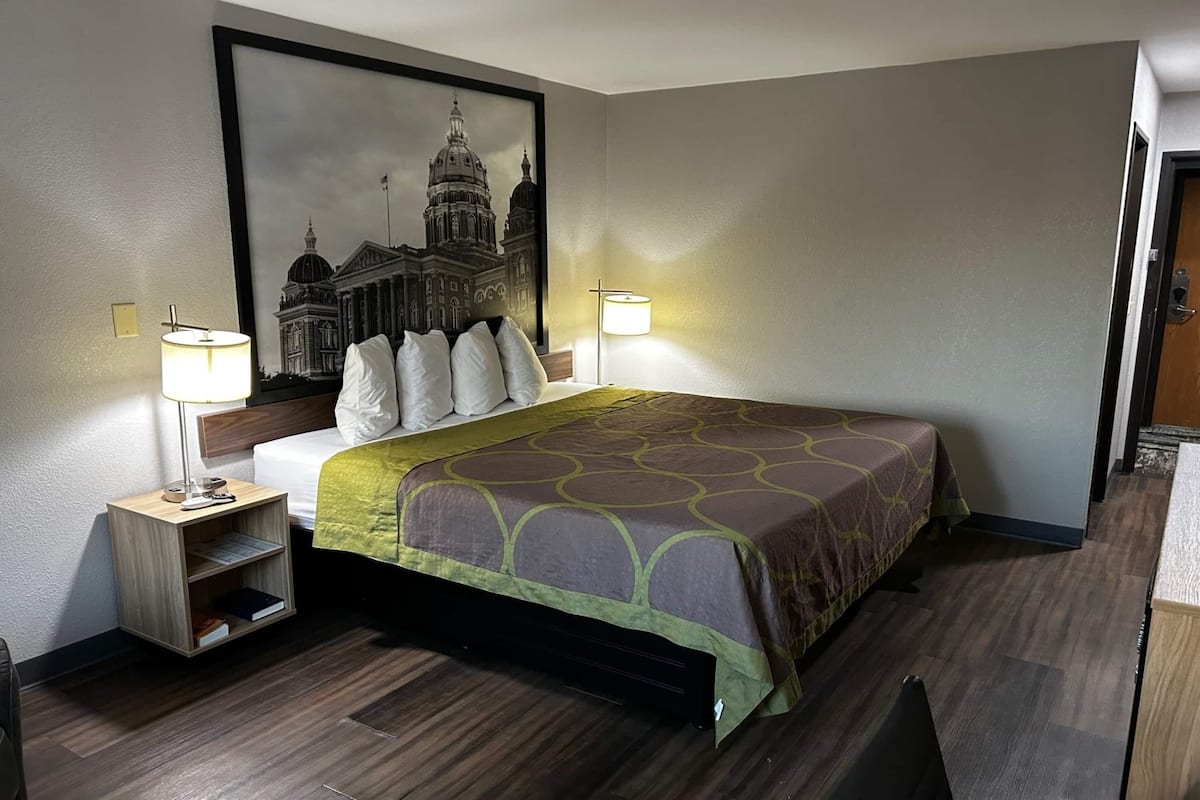 A hotel room with a large bed, two bedside lamps, a nightstand with a lamp, a framed picture on the wall, and a wooden floor.