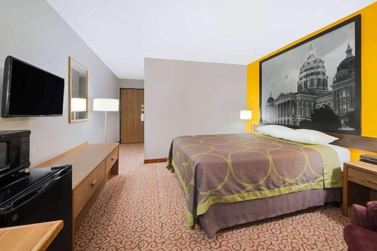 A hotel room with a bed, a television, a desk, a lamp, and a framed picture on the wall.