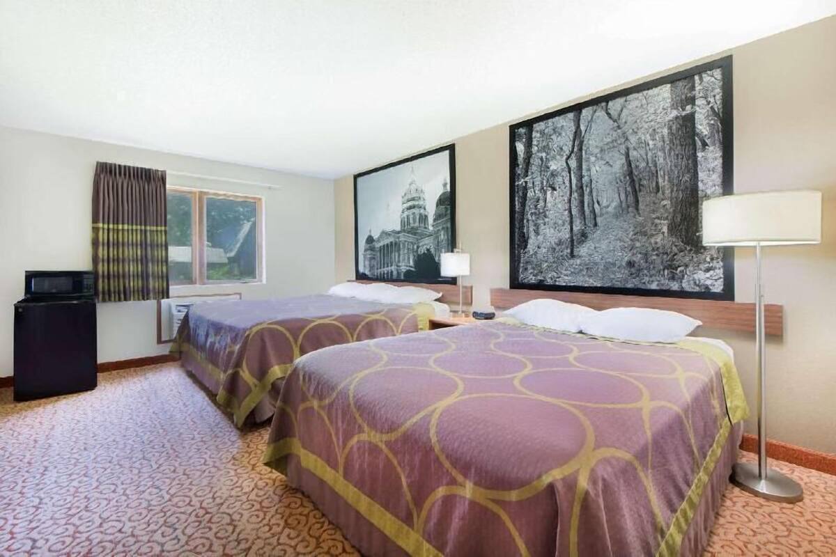 A hotel room with two beds, a large window, a flat-screen TV, and a painting of a forest.