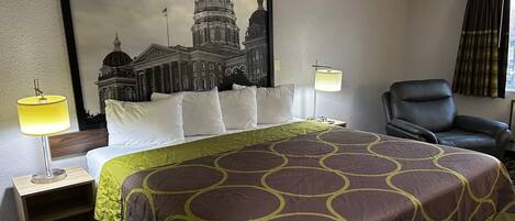 A hotel room with a large bed, two bedside lamps, a leather chair, and a framed cityscape picture on the wall.