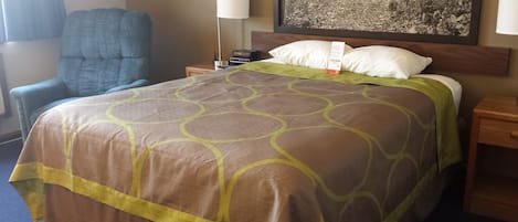 A hotel room with a bed, a chair, a nightstand, a lamp, and a painting on the wall.