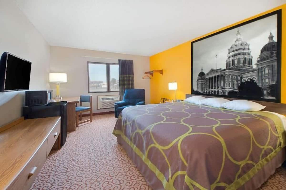 A hotel room with a bed, a desk, a chair, a TV, a window, and a wall-mounted lamp.