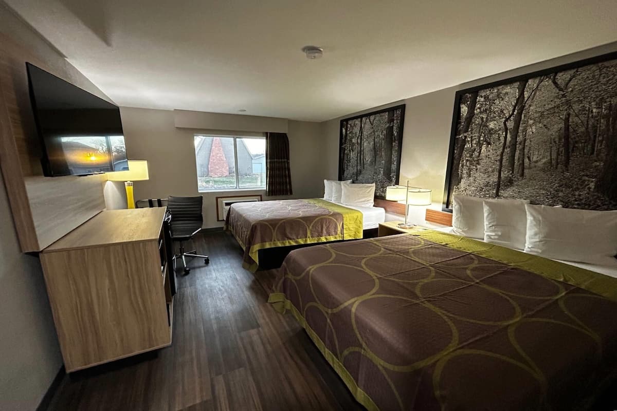 A hotel room with two beds, a desk, a chair, a TV, and a window with a view of a building.