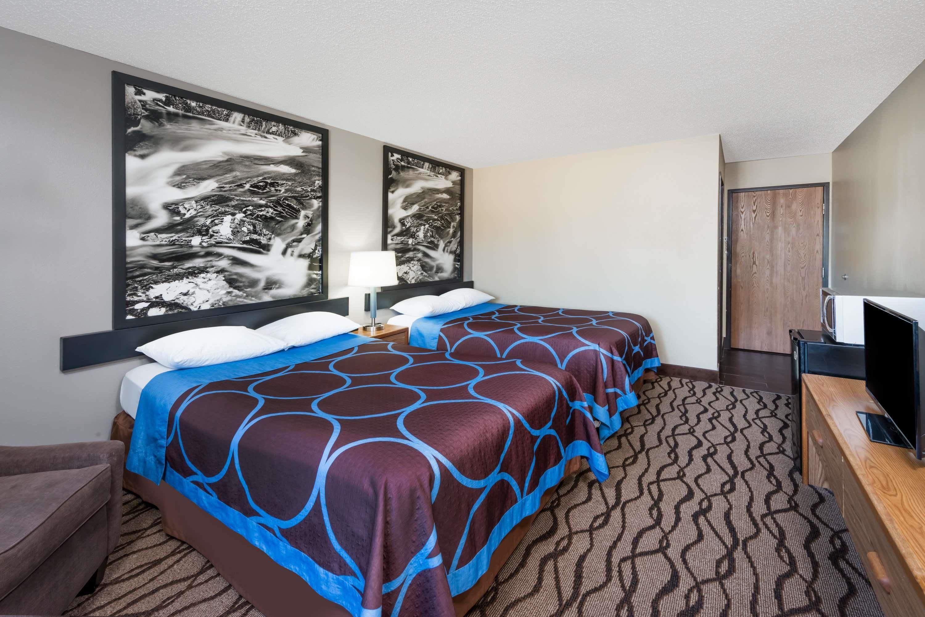 Una habitación de hotel con dos camas, televisión, escritorio y obras de arte en las paredes.