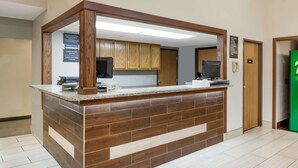 A reception area with a wooden counter, a check-in/out desk, and a sign with operating hours.
