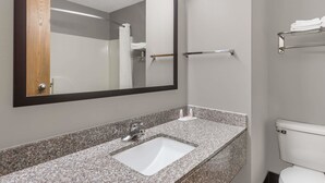A bathroom with a granite countertop sink, a mirror, a towel rack, and a toilet.