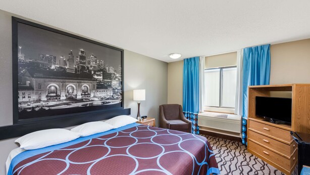 A hotel room with a large bed, a television, a desk, and a cityscape painting on the wall.