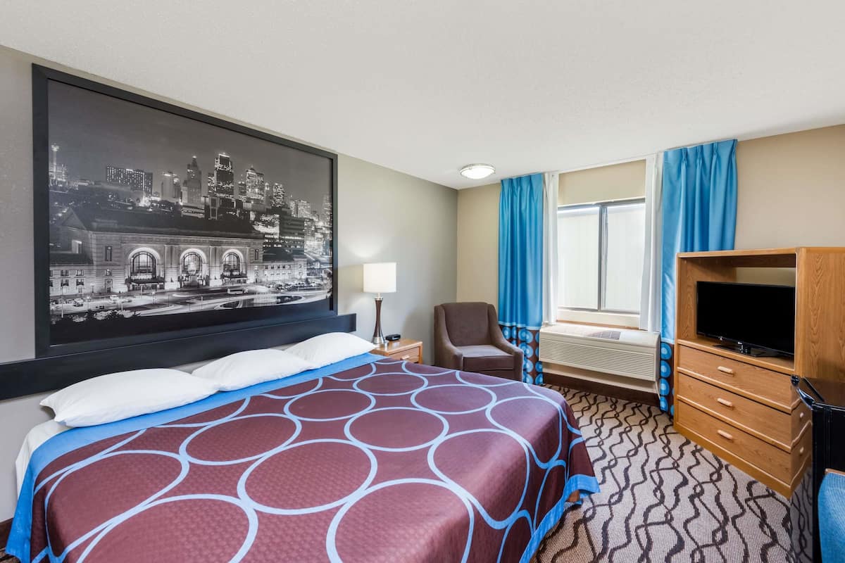 A hotel room with a large bed, a television, a desk, and a cityscape painting on the wall.