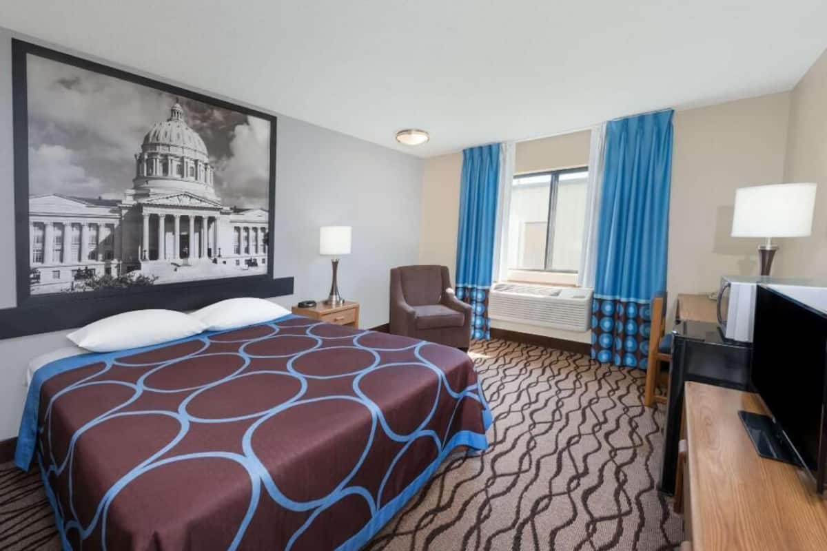 A hotel room with a large bed, a desk, a chair, a television, and a window with curtains.