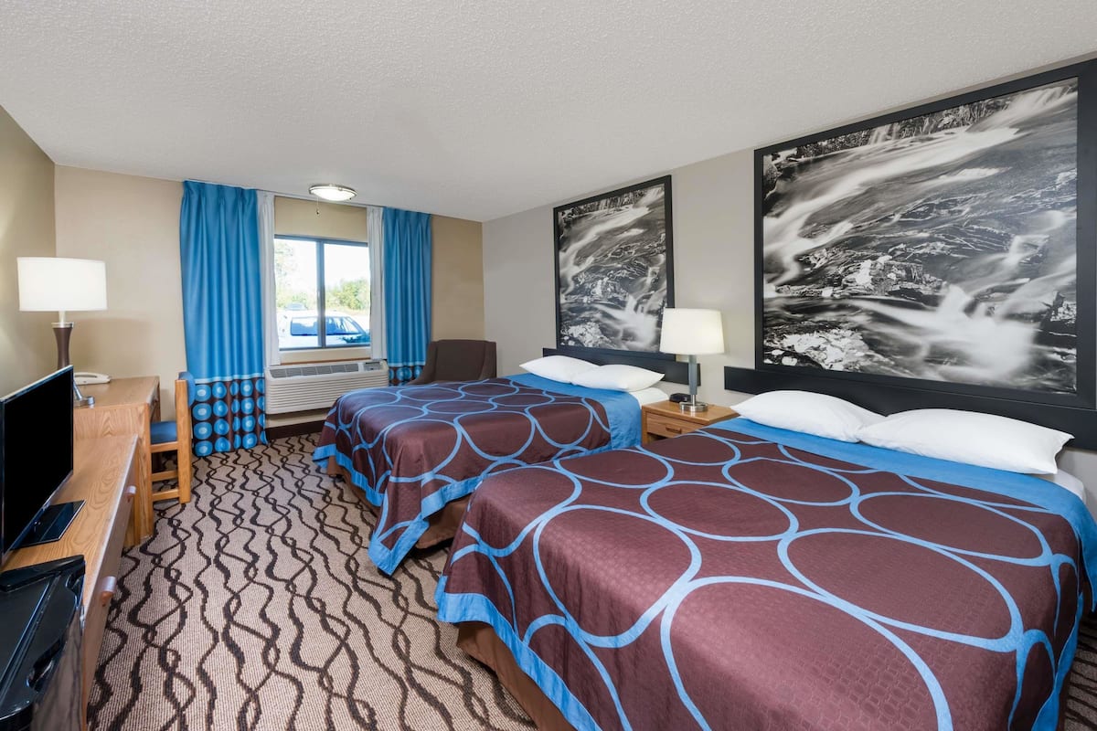 A hotel room with two beds, a desk with a computer, a chair, and a large window with curtains.