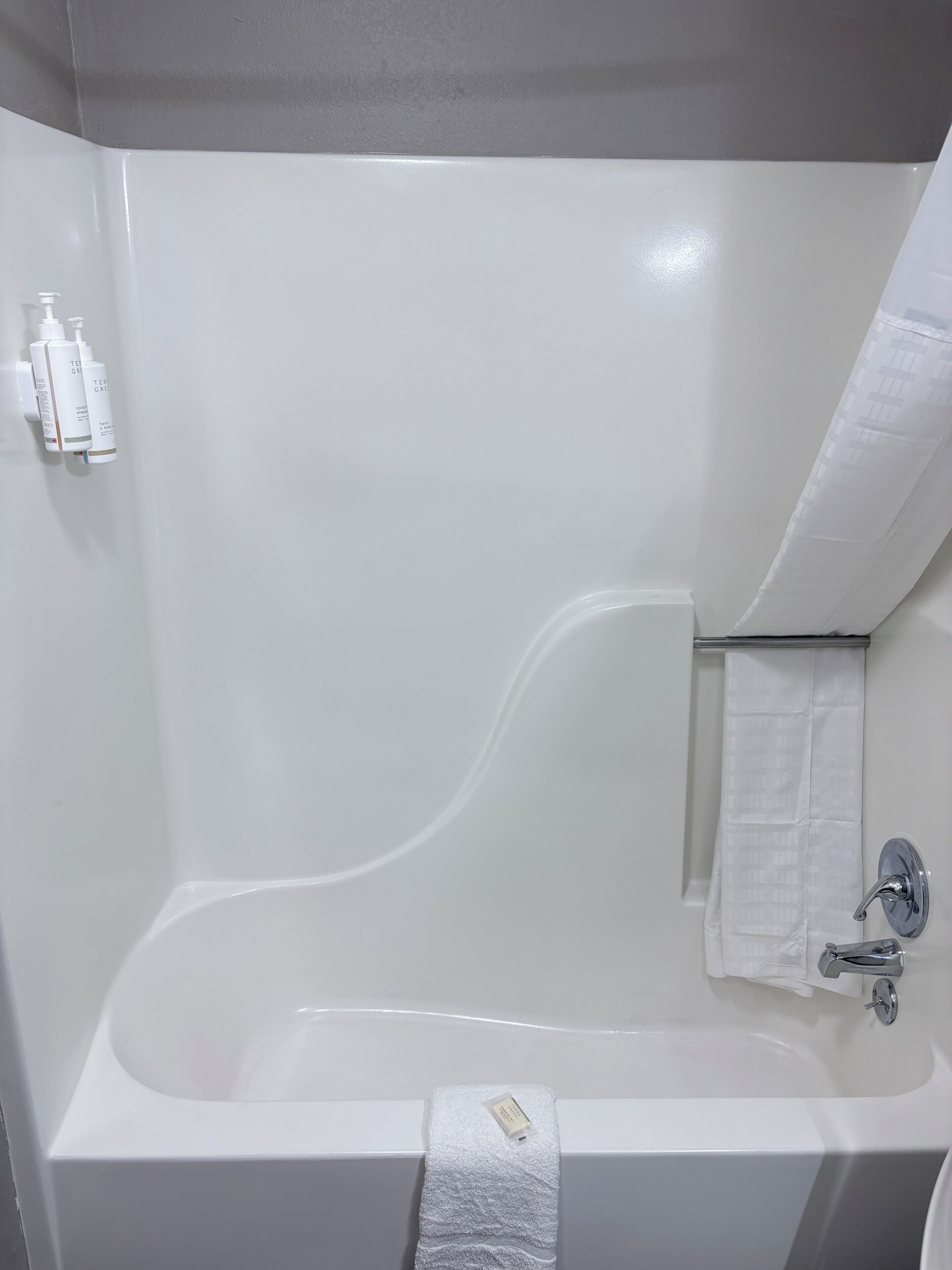 A white bathtub with a shower curtain, a towel, and toiletries on a wall-mounted holder.