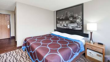 A hotel room with a bed, a nightstand, a lamp, a remote control, and a wall-mounted artwork of a cityscape.