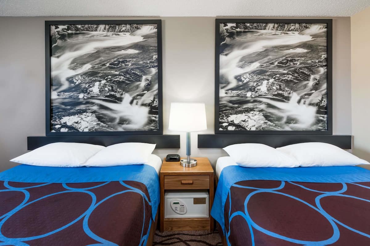 A hotel room with two beds, a nightstand with a lamp, and two large black-and-white photographs on the wall.