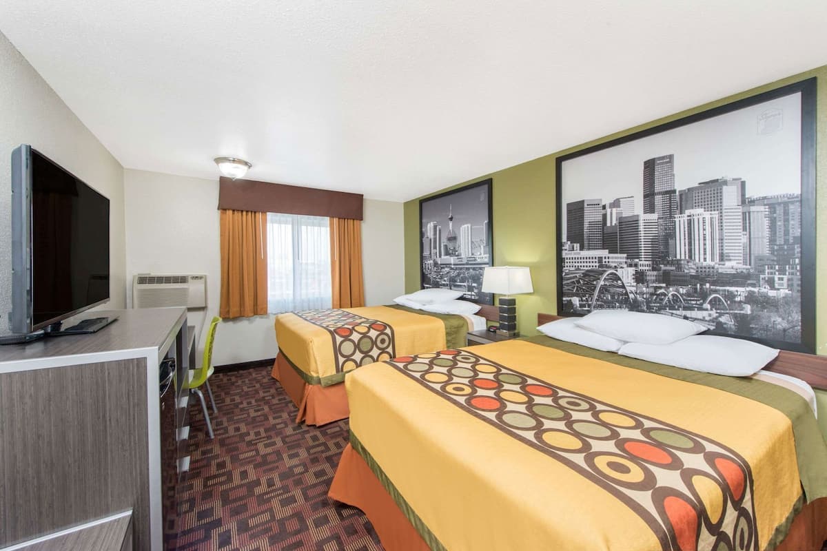 A hotel room with two beds, a television, a desk, and a cityscape painting on the wall.