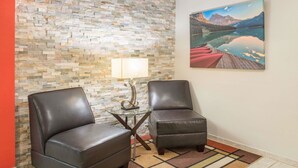 Une pièce comprenant deux fauteuils en cuir, une petite table avec une lampe, un tapis à motifs, un mur en pierre et un tableau représentant un paysage montagneux.