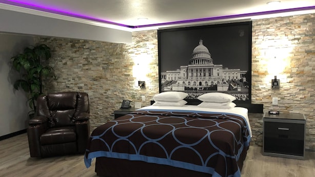 Une chambre à coucher comprenant un lit, un fauteuil en cuir, une table de chevet et un téléviseur fixé au mur.