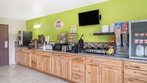 Un bar où l’on peut prendre le petit-déjeuner, avec un mur vert, un téléviseur à écran plat et divers produits pour le petit-déjeuner.