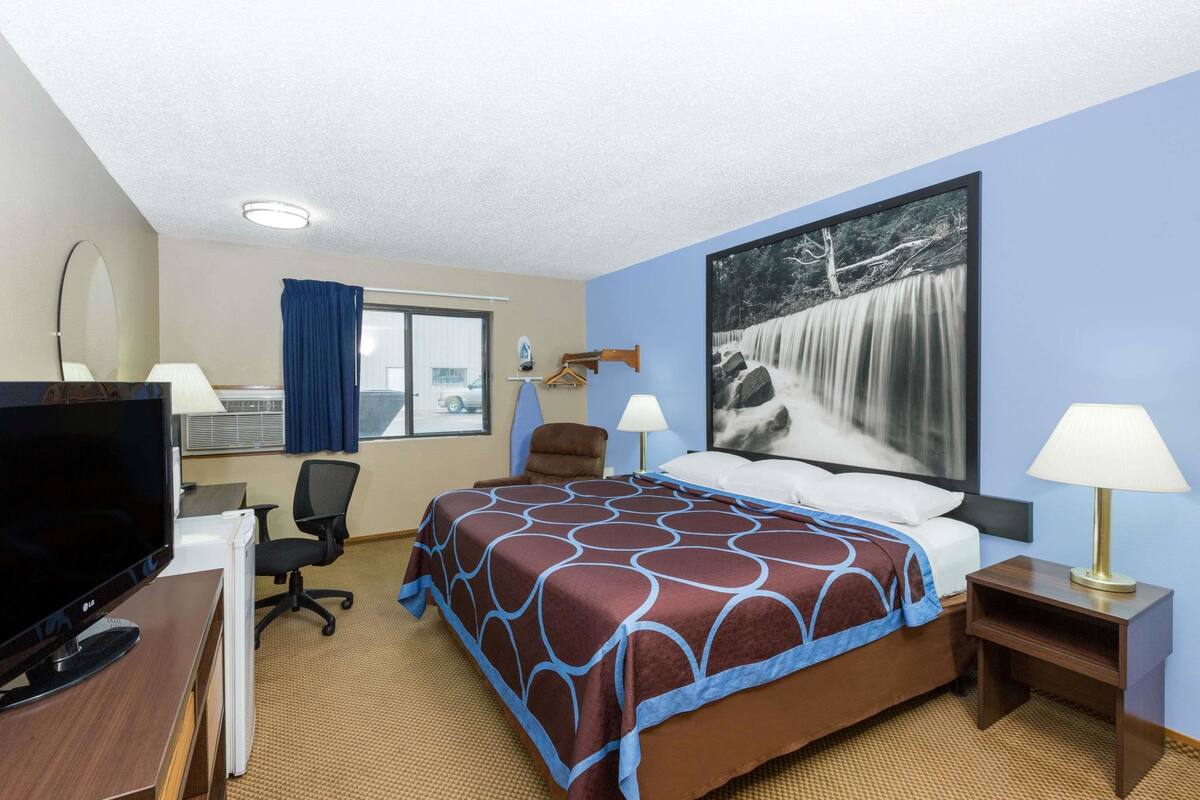 Una habitación de hotel con una cama, un escritorio con ordenador, una silla y un televisor.