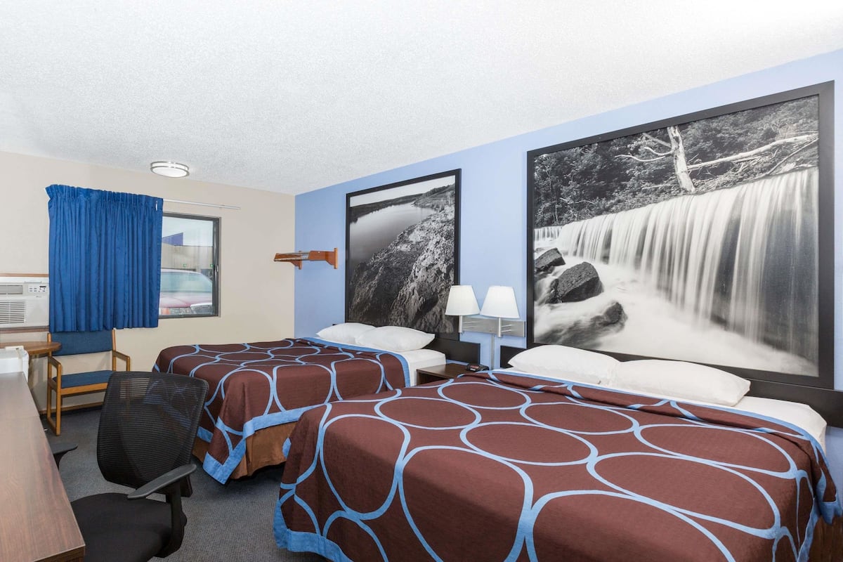 Habitación de hotel con dos camas, un escritorio, una silla y un cuadro grande de una cascada en la pared.