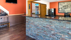 Een receptiezone met een stenen balie, een aan de muur bevestigde televisie en een houten deur naar een bibliotheek.