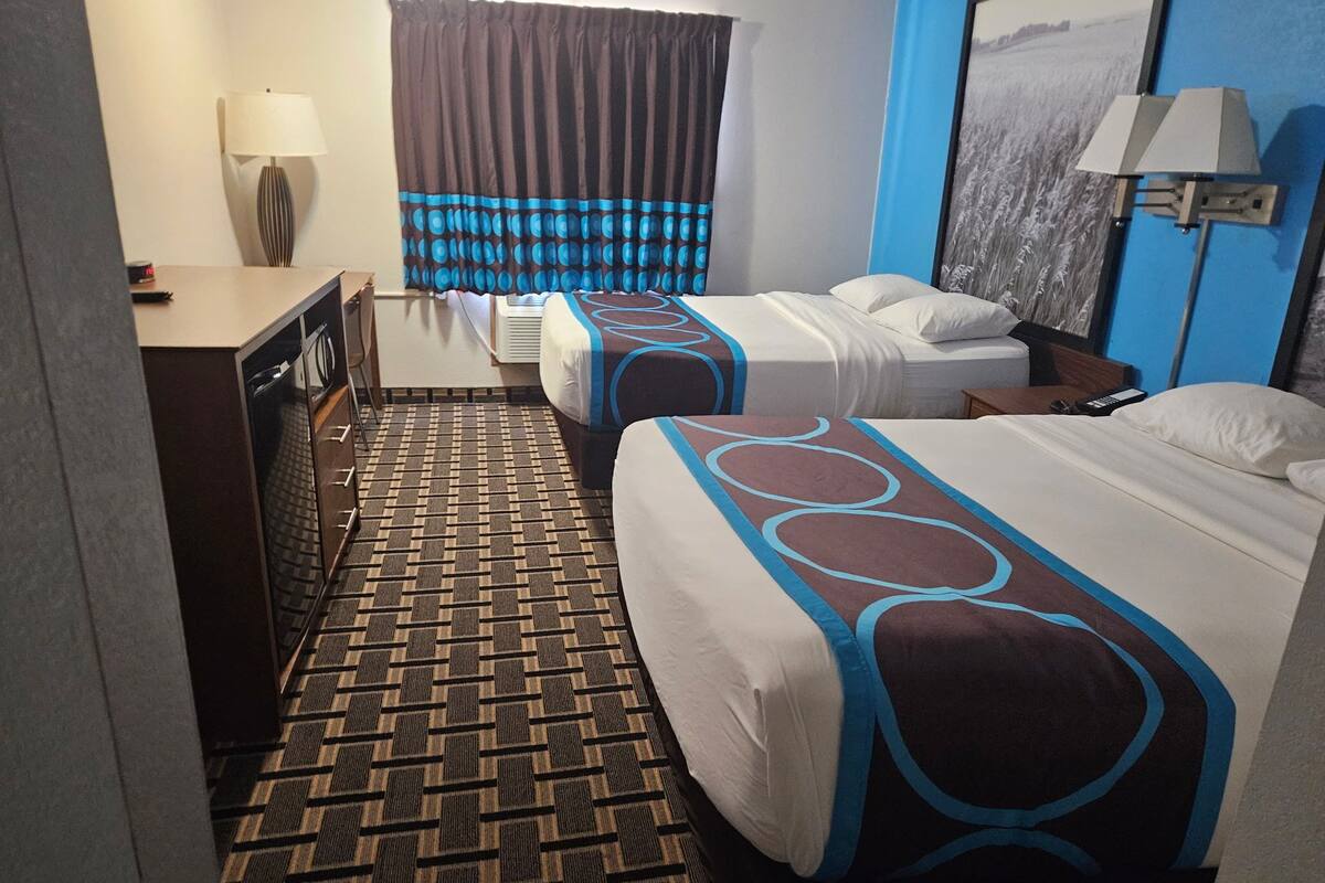 Een hotelkamer met twee bedden, een bureau, een lamp en een schilderij aan de muur.